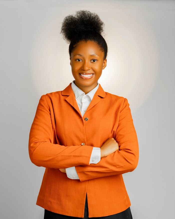 services-01 Portrait of a confident African businesswoman smiling while wearing a vibrant orange jacket, standing with arms crossed.