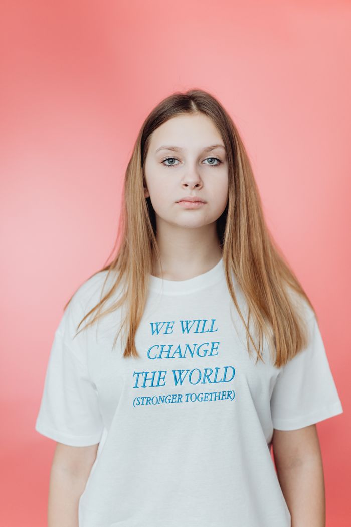 Young woman wearing a motivational text t-shirt, posing against a pink background.