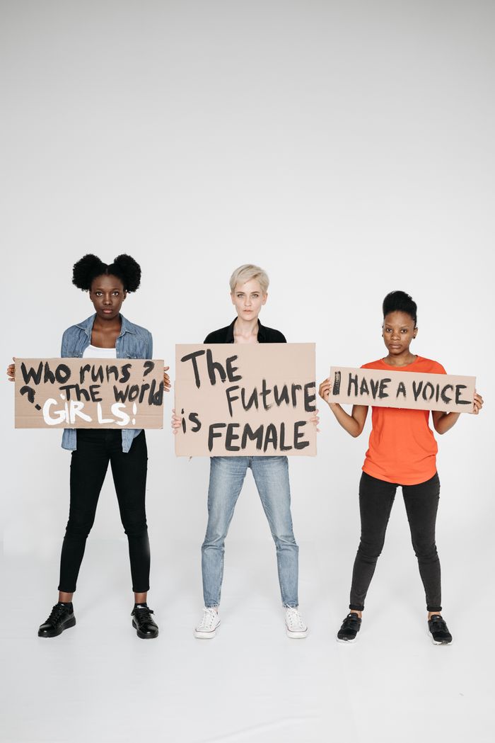 services-02 Three diverse women standing with empowering feminist protest signs on a white background.